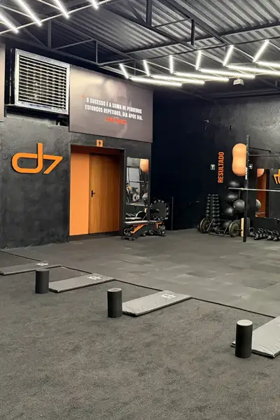 Entrada do salão do CT D7 com logo laranja, porta e racks de treino