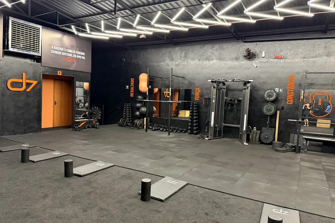 Panorama do salão de treino do CT D7 com logo laranja, iluminação em LED e equipamentos